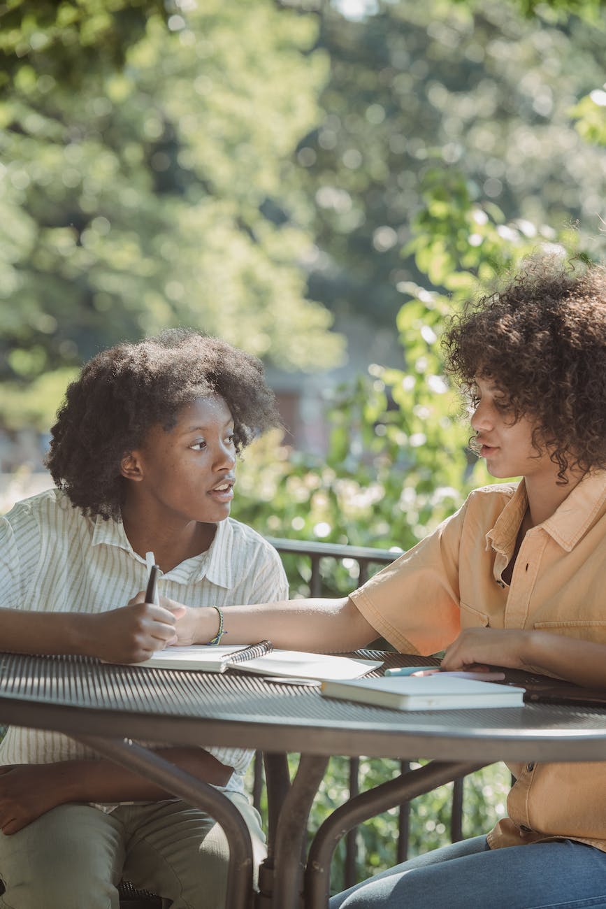 girls with curly hair making notes at a table in a park