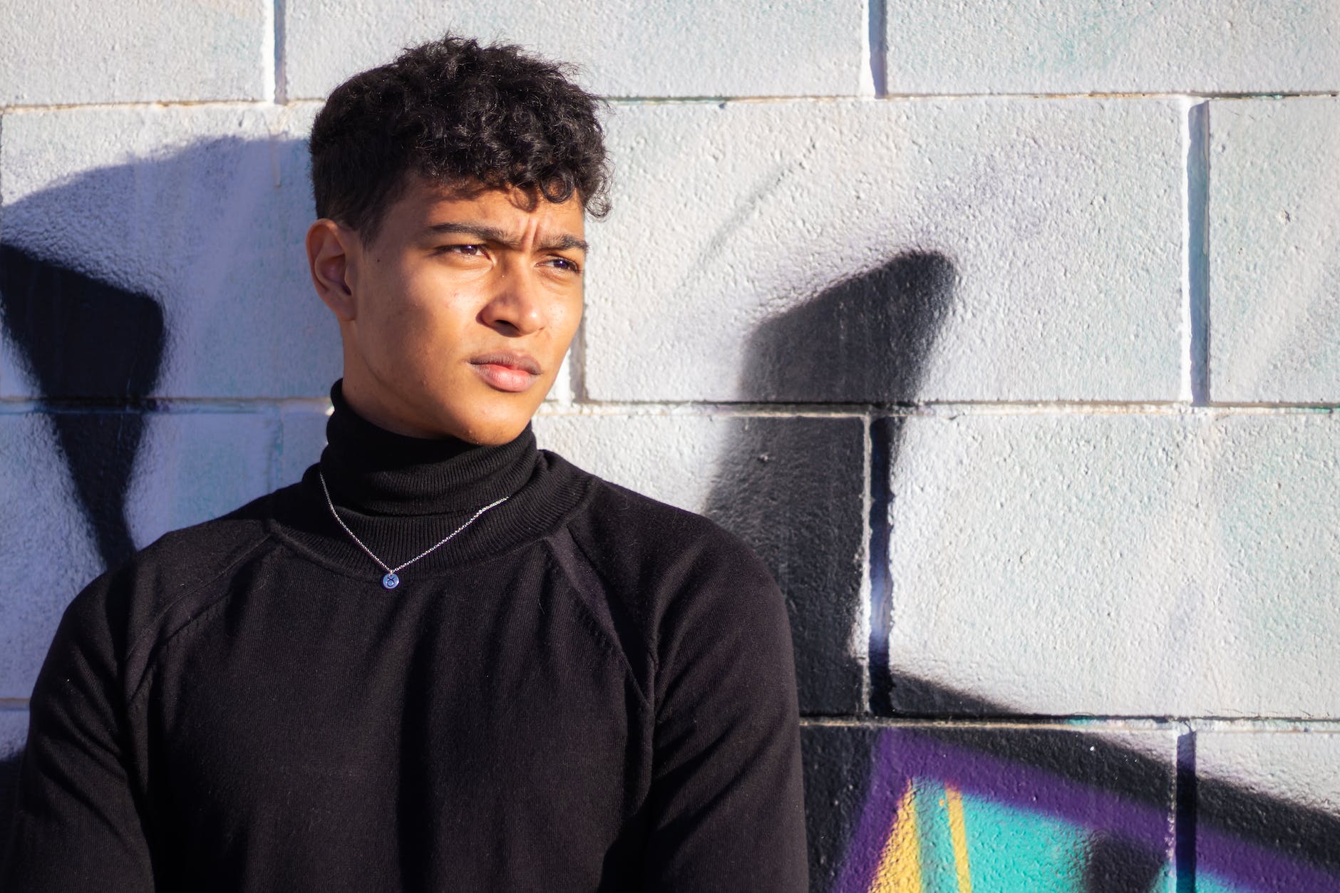 man in turtleneck shirt beside concrete wall