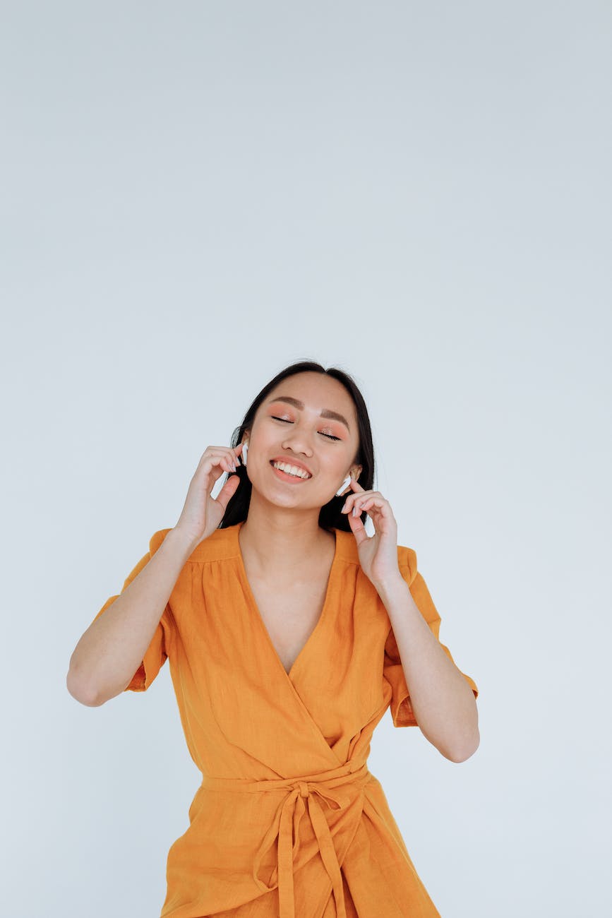 a happy woman in orange dress listening to music on her wireless earphones