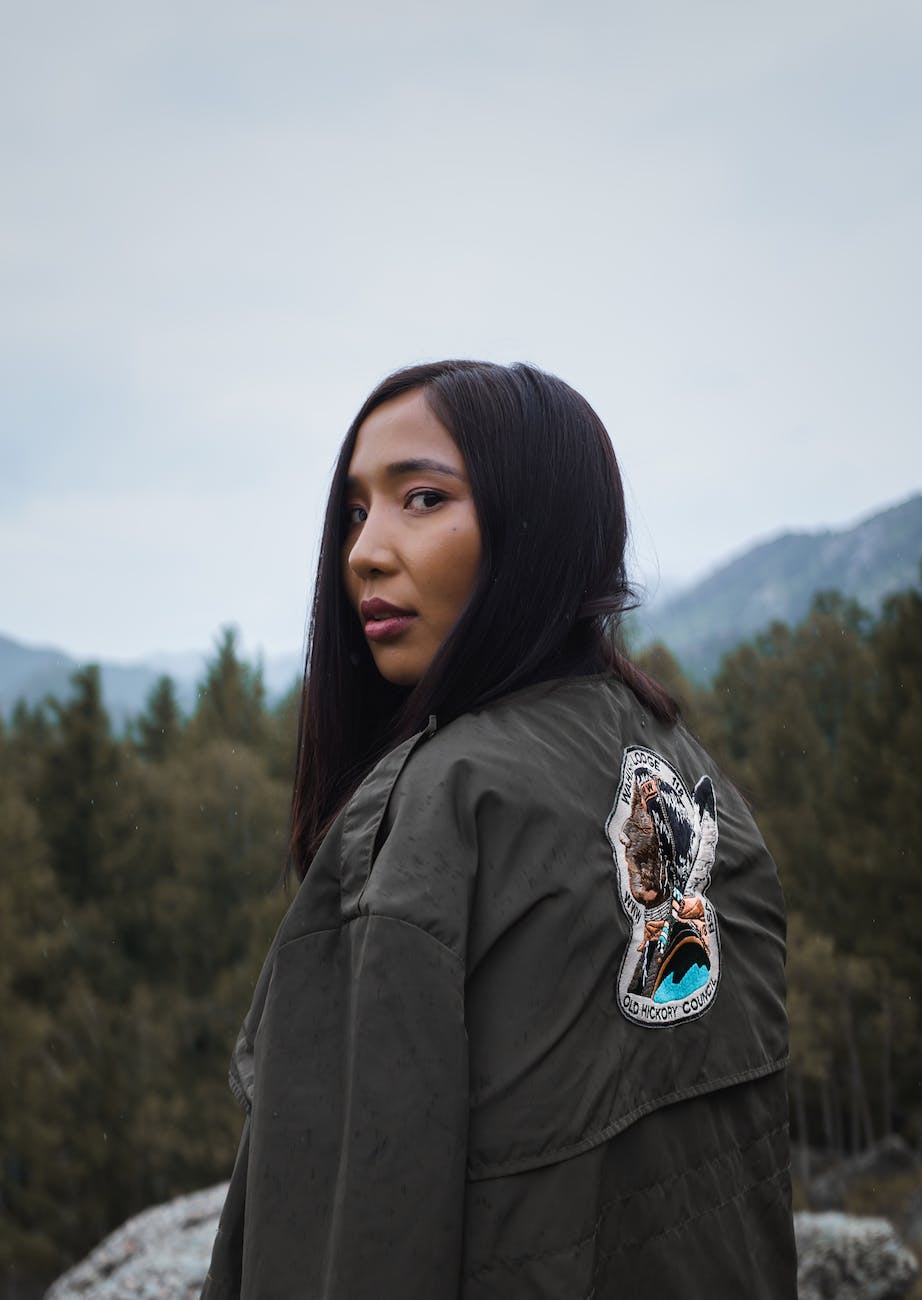 ethnic woman standing behind mountains under cloudy sky in countryside